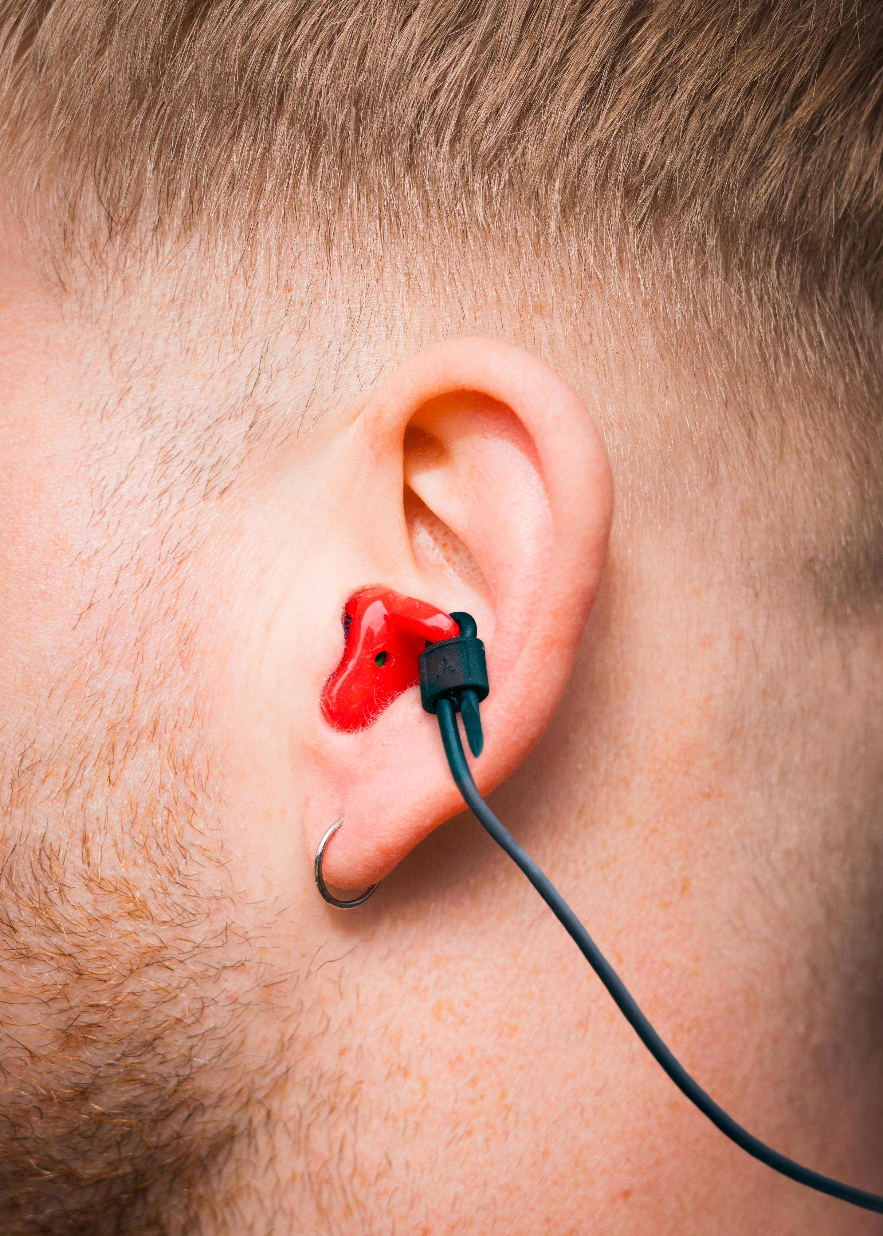 Alpine WorkSafe Custom Red earplug with black cord worn in a man&