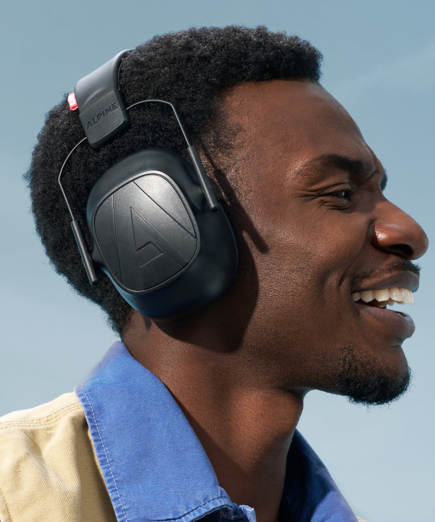 Alpine Defender earmuffs worn by a smiling man in a blue shirt and beige jacket 